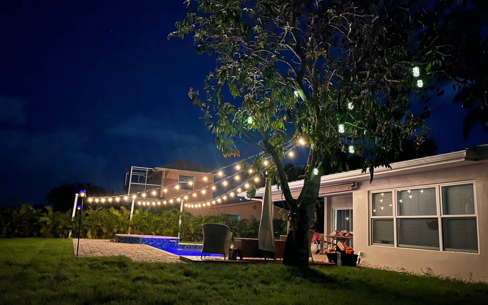 Backyard with string lights and a paver pool deck at night