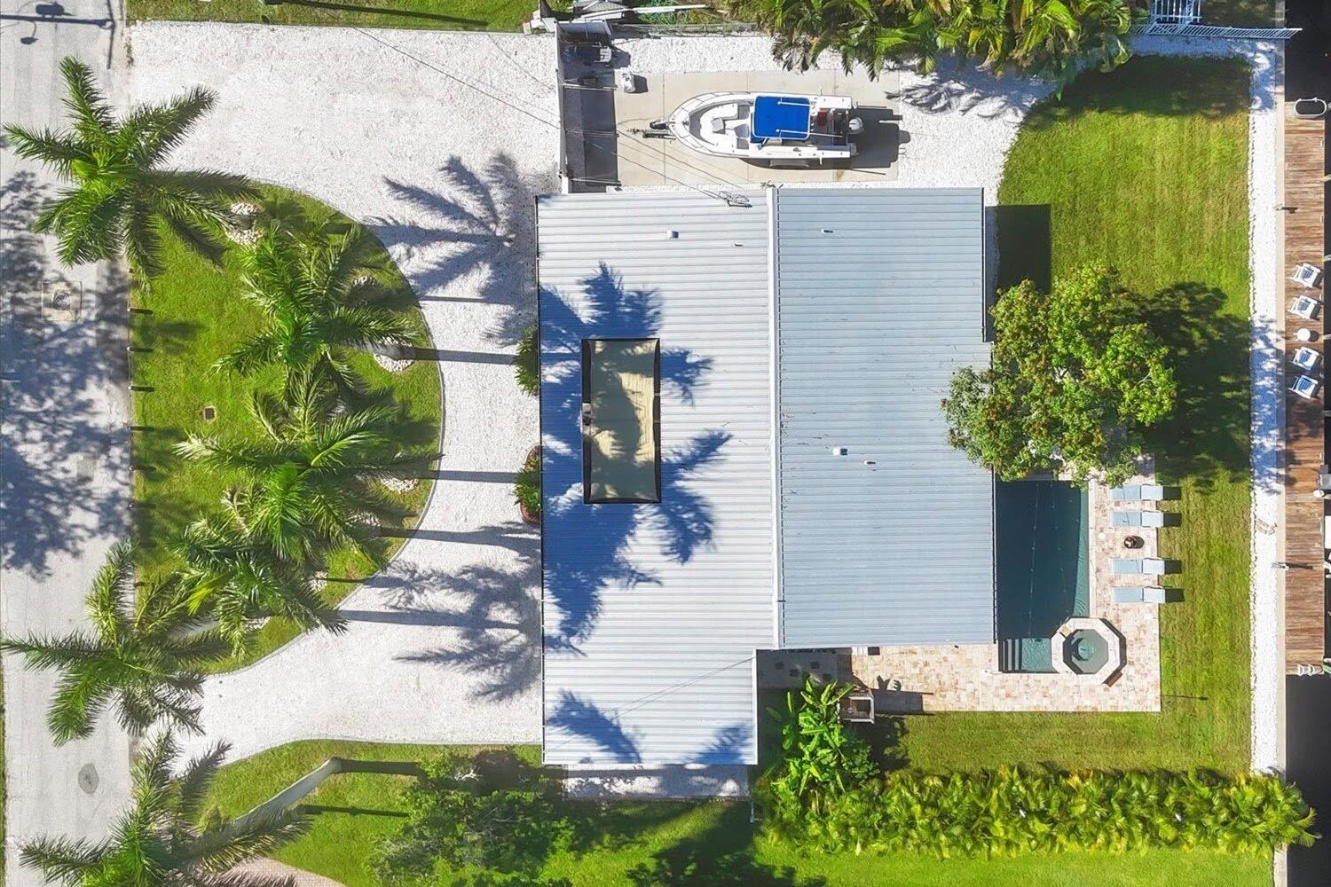 Aerial view of a canal-front home with a shell driveway, palms, lawn and dock
