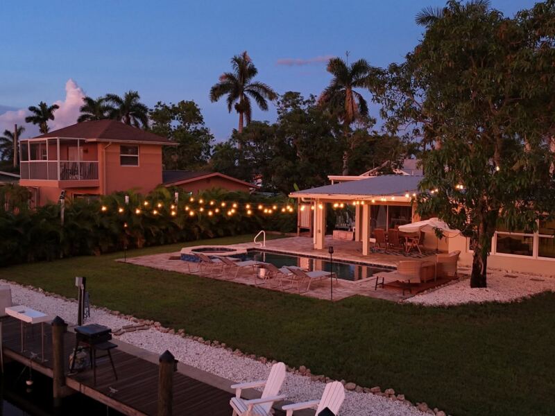 Canal-front backyard at dusk with string lights, pool and new lawn
