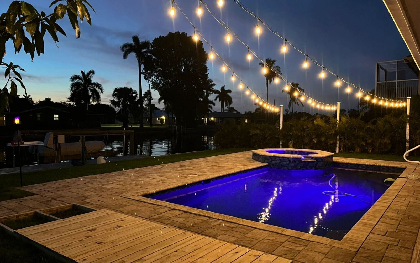 Paver pool deck with string lights at dusk