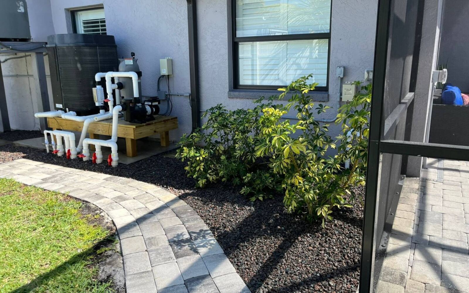 Side-yard beds with dark rock and shrubs beside a curved paver walkway
