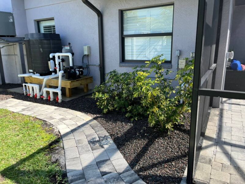 Side-yard beds with dark rock and shrubs beside a curved paver walkway